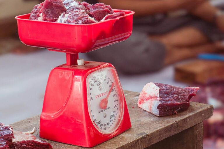 Raw meat being weighed on a red kitchen scale